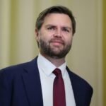 Retrato de J.D. Vance durante una conferencia, vestido con traje oscuro, expresando con seriedad y énfasis.