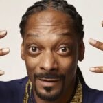 Snoop Dogg con gafas oscuras y trenzas, en el escenario durante un show en vivo.